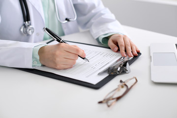 Fototapeta premium Close-up of a female doctor filling out application form , sitting at the table in the hospital