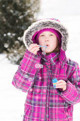 Little girl blowing bubbles outdoors in snow