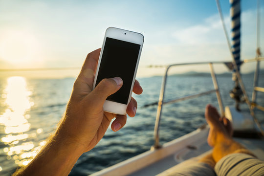 Summer leisure. Rest on a yacht with a phone in his hand. Man lying on the deck and enjoy your smartphone. The guy doing the photo feet on the background seascape and yachts.