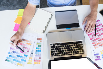 Top view of a young graphic designer working on a desktop computer and using some color swatches, top view