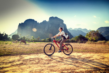Fototapeta na wymiar Happy tourist woman riding a bicycle in mountain area in Laos. Travelling in South East Asia