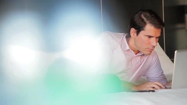 Man reclining on bed using laptop computer