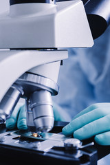 Close up view of scientist hands with gloves set the sample in the microscope for research