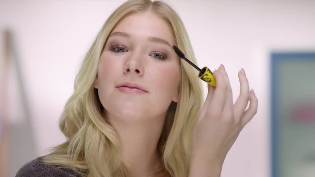 Young caucasian woman applys mascara at her eyelashes