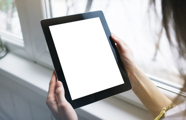 Hipster person hands holding digital tablet with empty blank screen, against a background of  window horizontal,  freelancer girl using at home on a computer on the balcony, mockup teghnology,  blur