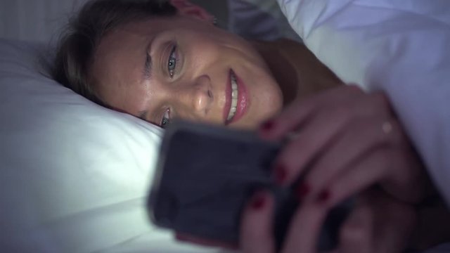 Woman using multimedia smartphone in bed