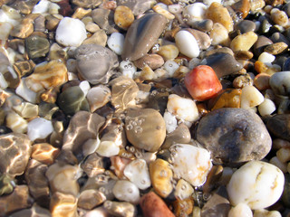 Background from colorful sea pebbles, water and foam.