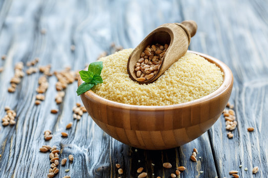 Wooden scoop with grains of wheat in a bowl with couscous.