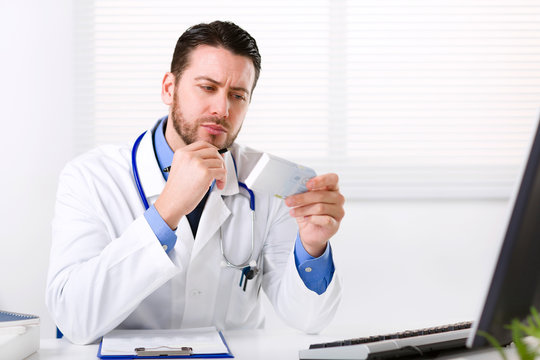 Male Doctor Reading Medicine Label Of Medicine Box