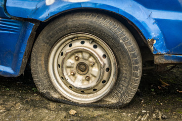 Flat tire part of an abandoned blue car parked in garden photo taken in Depok Indonesia