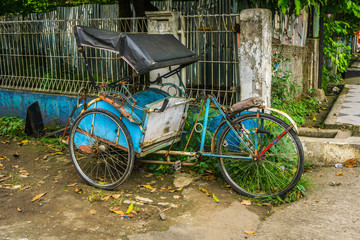Fototapeta na wymiar Blue pedicap or tricycle parked in side of the road near bush and wall with nobody around photo taken in Depok Indonesia