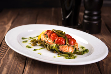 Grilled trout with tomatos leguminous beans and lemon on white plate wooden background. Top view