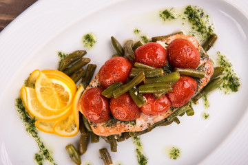 Grilled trout with tomatos leguminous beans and lemon on white plate. Top view close up