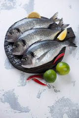 Cutting board with raw sea breams on a white concrete background