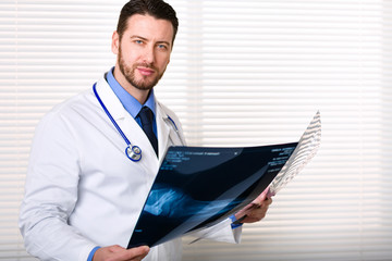 Handsome male doctor portrait with stethoscope on his neck standing while holding patients x-ray;...