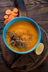 Blue bowl with carrot cream-soup on a rustic wooden background