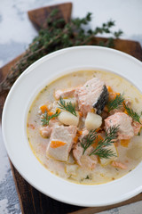 Fish soup with salmon served in a white glass plate, close-up