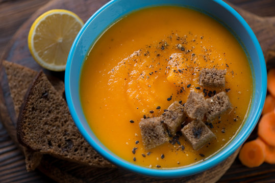 Carrot cream-soup served in a blue bowl with croutons, closeup