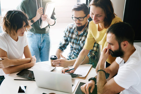 Group of friends is planning new journey by using a route application on a laptop. Young hipsters are discussing latest technology news after reading it in the internet on a laptop.