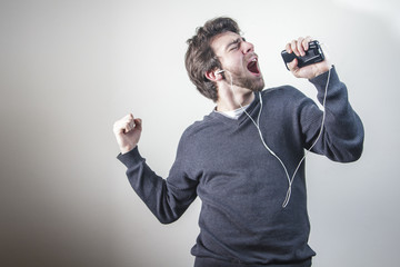 Young man dancing and singing to the music on his mobile phone through earphones, goofy and happy