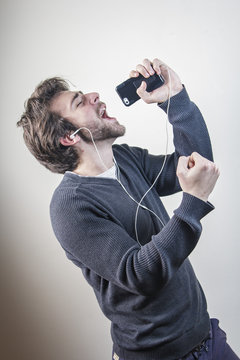 Young Man Dancing And Singing To The Music On His Mobile Phone Through Earphones, Goofy And Happy