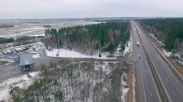 Highway view from a height, winter forest and field, the traffic cars on the highway, gas station. 
