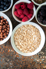 Oat, raspberries, red currant, blueberries, blackberries, chocolate balls in bowls on a rusty background