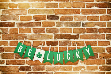 BE LUCKY handmade garland letters on rustic orange wall background. Bright St. Patricks day holiday potcard, banner, greeting card, poster template. Irish national colors. Green clover leaf.