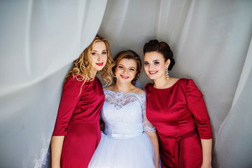 Naklejka premium Cute blonde bride with bridesmaids posed on curtains at wedding morning day.