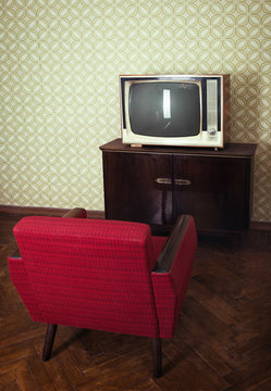 Vintage room with old fashioned red armchair and retro tv over obsolete wallpaper, image toned.