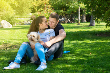 Obraz premium Young couple with puppy. Portrait of attractive happy smiling young woman and man holding cute little dog, summer park outdoor.