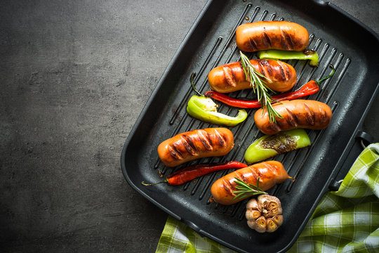 Fried sausages with  vegetables in grill pan at black background