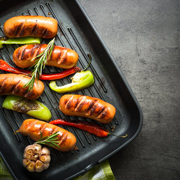 Fried sausages with  vegetables in grill pan at black background