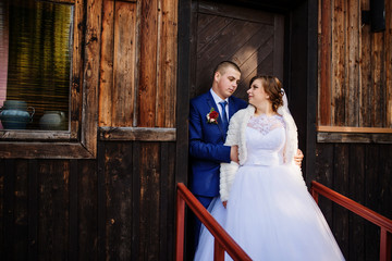 Wedding couple against old wooden house with red leaves on his.