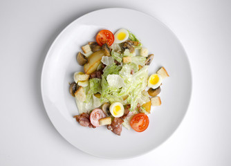 Salad with fried bacon and vegetables on a white plate on a white background
