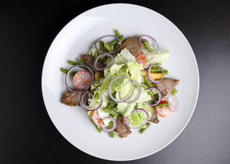 Salad with beef roast beef and vegetables on a black background