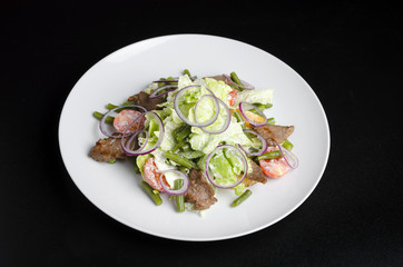 Salad with beef roast beef and vegetables on a black background