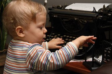 Little boy playing with typewriter and Newtons cradle