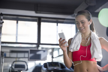 Cheerful beautiful young woman listening to music in the gym