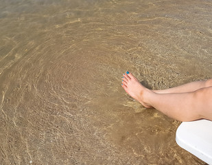 Woman's leg lay on the white armchair on the beach
