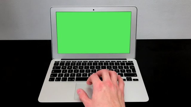 Man's hand using and scrolls track pad laptop in the front view. Computer, notebook with chromakey on a black table in a room with white wall. 4k video.