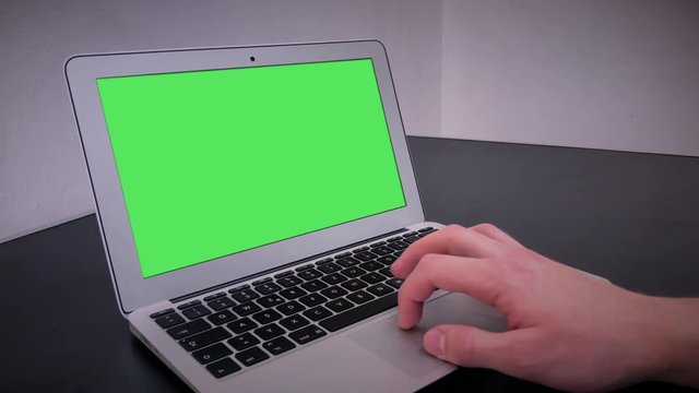 Man's hand using and scrolls track pad laptop. Computer, notebook with chromakey a three-quarter view on a black table in a room with white walls. 4k video.