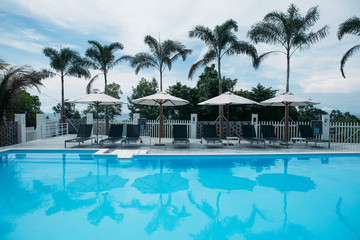 Beautiful tropical beach front hotel resort with swimming pool, sun-loungers and palm trees during a warm sunny day, paradise destination for vacations