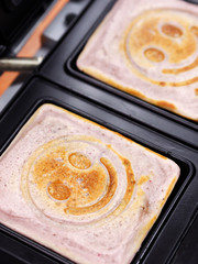 Close up smiley blueberry pancakes cooking on sandwich maker