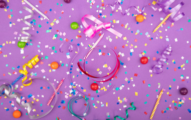 Colorful party attributes with streamers, confetti and horns over lilac background. Flat lie. High resolution photo.