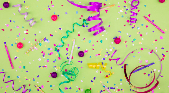 Colorful party attributes with streamers, confetti and horns over GREEN background. Flat lie. High resolution photo.
