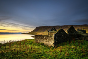 Scenic landscape including ruined house, typical cliffs and a lake in Iceland