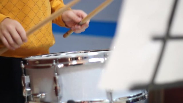 Young musician playing drum reading sheet music during funny school fair. Focus on the hands