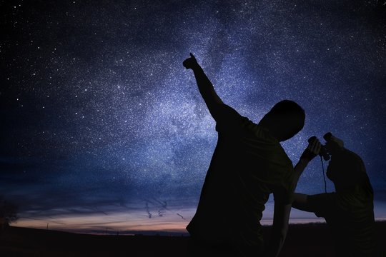 Silhouettes of people observing stars in night sky. Astronomy concept.