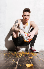 Bad man with tattoo eating potato chips from the packet
